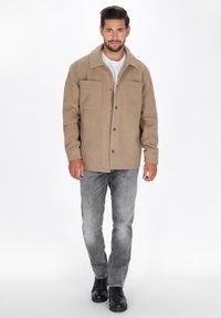 Beige wollen blend jas met een kraag, drukknoopsluiting aan de voorkant, twee borstzakken en lange mouwen, gecombineerd met grijze jeans en zwarte laarzen.