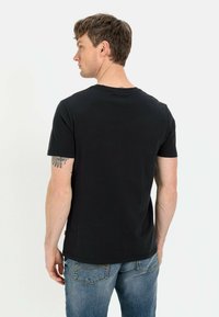 Sort kortærmet t-shirt lavet af bomuld, med rund hals og regular fit, båret med falmede blå jeans. Viset fra ryggen.