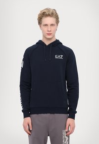 Tengerészeti kapucnis pulóver hosszú ujjakkal, elülső zsebével és húzózsinórral. EA7 márkajelzés található a mellkason és a bal karon fehér színben. Puha szövet textúrával.