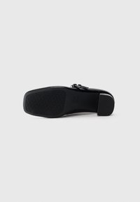 Black leather dress shoe shown from sole side with textured grip and low block heel on plain white background.