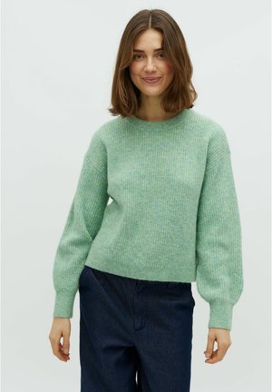 Pulover tricotat verde deschis, cu mâneci lungi ușor puffate și textură cu nervuri. Asortat cu pantaloni largi de culoare albastră închis.