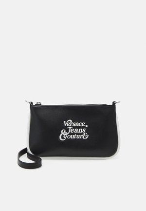 Schwarze rechteckige Umhängetasche mit weißem Besatz und Versace Jeans Couture-Logo in weißer Schrift auf der Vorderseite.
