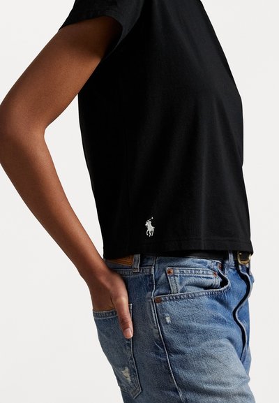 Black cotton t-shirt with a classic fit, short sleeves, and a white embroidered logo at the bottom hem, paired with distressed blue jeans.