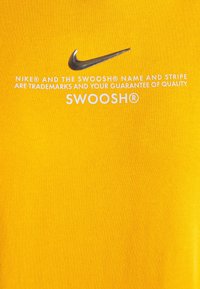 Geel katoenen T-shirt met een metallic Nike Swoosh-logo en witte tekst die de merkhandelsmerken en kwaliteitsgarantie vermeldt.