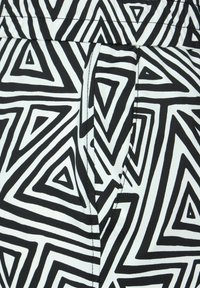 Detailní záběr černobílého geometrického vzoru s trojúhelníky na látce s detailem švu kapes.