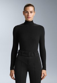 Fekete, hosszú ujjú felső, magas nyakú, sima anyagból készült; magas derekú nadrággal párosítva, amelynek struktúrált, texturált öve van.