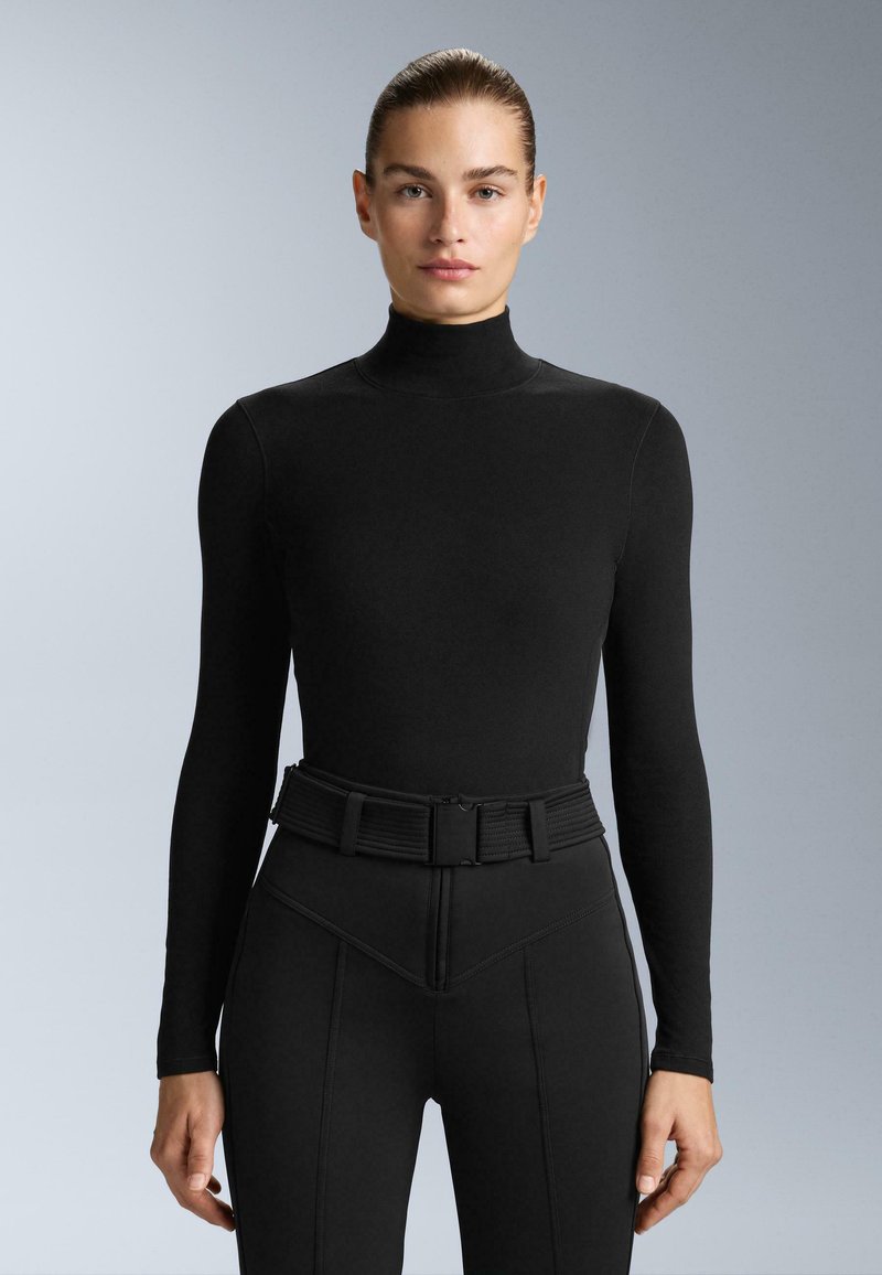 Fekete, hosszú ujjú felső, magas nyakú, sima anyagból készült; magas derekú nadrággal párosítva, amelynek struktúrált, texturált öve van.