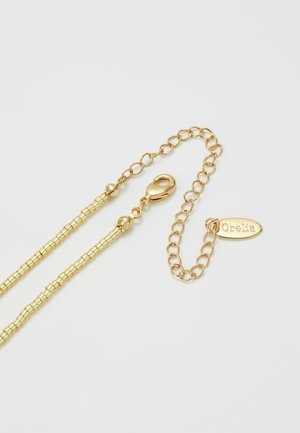 Collier chaîne réglable ton or avec fermoir mousqueton et étiquette ovale gravée « Orelia » sur fond blanc.