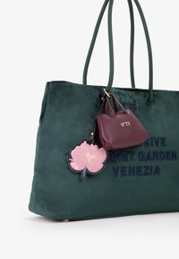 Borsa tote in suede verde con testo ricamato. Presenta un'applicazione floreale rosa e una piccola pochette in pelle bordeaux attaccata a un manico.