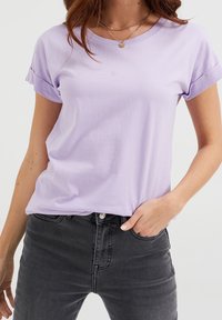 Ljuslila kortärmad T-shirt i mjuk bomull. Har rund hals och upprullade ärmslut. Kombineras med mörkgrå denimjeans.