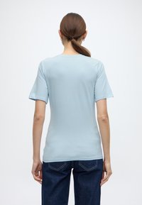 Ανοιχτό μπλε βαμβακερό μπλουζάκι με κοντά μανίκια, στρογγυλή λαιμόκοψη και εφαρμοστή σιλουέτα, σε συνδυασμό με σκουρό μπλε τζιν παντελόνι.