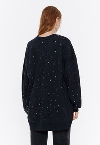 Sudadera negra de corte holgado, con mangas largas y adornos decorativos multicolores esparcidos por toda la tela.