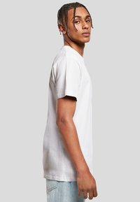 White short-sleeve cotton t-shirt with a crew neckline, featuring a relaxed fit and soft texture. Worn with light blue denim jeans.