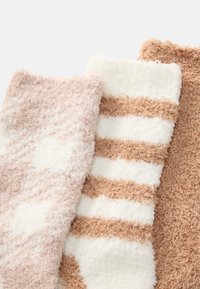 Tre par plyssokker: et i lys rosa, et med hvide og brune striber, og et i ensfarvet brun, alle med en blød og fluffy tekstur.