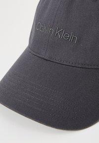 Boné de beisebol preto feito de tecido texturizado, com um logótipo bordado "Calvin Klein" em fio escuro na parte da frente.