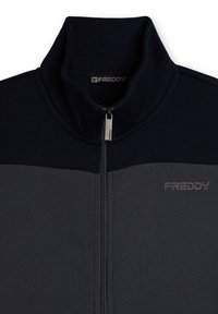 Chaqueta de forro polar azul oscuro y gris con cremallera y cuello alto, con cremallera plateada y logo "FREDDY" en el pecho. Textura suave y bloques de color.