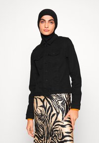 Veste en denim noire avec poches avant, fermeture à boutons et col. Assortie d'une jupe crémeuse et noire à motifs, avec des motifs de feuilles.
