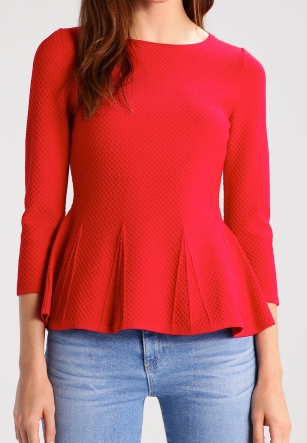 Haut peplum rouge avec un motif texturé, encolure ronde et manches trois-quarts, associé à un jeans bleu clair.