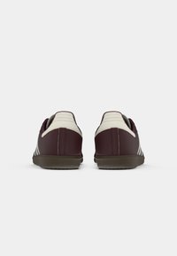 Et par mørkerøde sneakers med hvid hælkonstruktion og brune strukturerede såler, set fra bagsiden på en hvid baggrund.