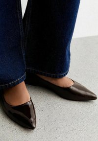 Brown patent leather pointed-toe flats with a low heel, paired with dark blue wide-leg jeans. Smooth texture with a glossy finish.