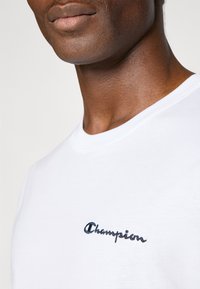 Hvid bomulds t-shirt med rund halsudskæring og korte ærmer, fremhævet af et mørkeblåt broderet "Champion" logo på brystet.
