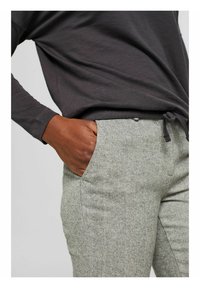 Camicetta grigia a maniche lunghe parzialmente visibile sopra pantaloni grigi chiari a motivo herringbone con tasca frontale e vita con coulisse.