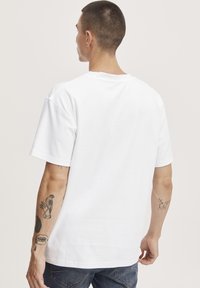 Witte katoenen T-shirt, standaard pasvorm, korte mouwen, ronde hals, eenvoudig ontwerp, gladde textuur, gedragen met blauwe spijkerbroek.