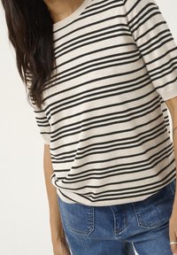 Haut en tricot rayé beige clair et noir avec des manches courtes, un col rond et une coupe décontractée, associé à un jean en denim bleu.