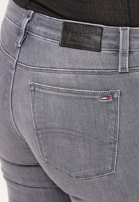 Jeans de denim gris con un bolsillo trasero prominente y una etiqueta de piel con la marca. Presenta costuras regulares y un pequeño acento tricolor cerca del bolsillo.
