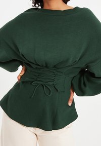 Grünes, geripptes Langarmoberteil mit lockerer Passform und tailliertem Detail. Verfügt über einen weiten Ausschnitt und gepuffte Ärmel, hergestellt aus weichem Stoff.