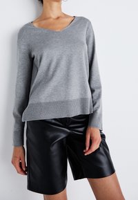 Harmaa neulepaita, jossa v-kaula-aukko ja resorit hihansuissa, yhdistettynä mustiin keinonahkahousuihin, joissa on sileä pinta ja väljähkö istuvuus.