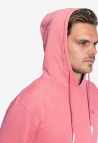 Lichtroze hoodie met een trekkoordcapuchon, voorzien van een zachte textuur en geribde manchetten. Geborduurd logo op de borst.