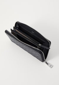 Černá kožená peněženka s texturovaným povrchem, zipovým uzávěrem a více přihrádkami na karty a hotovost. Obsahuje stříbrný zip a akcenty.