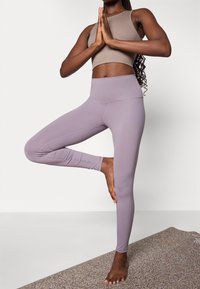 Light purple high-waisted leggings made of stretchy fabric, paired with a fitted brown ribbed crop top, worn by a person in a yoga pose.