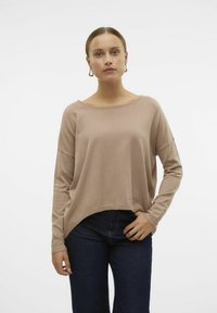 Pull en tricot beige clair avec un col large et arrondi et des manches longues, doté d'un ourlet légèrement incurvé et de poignets côtelés. Associé à un jean foncé.
