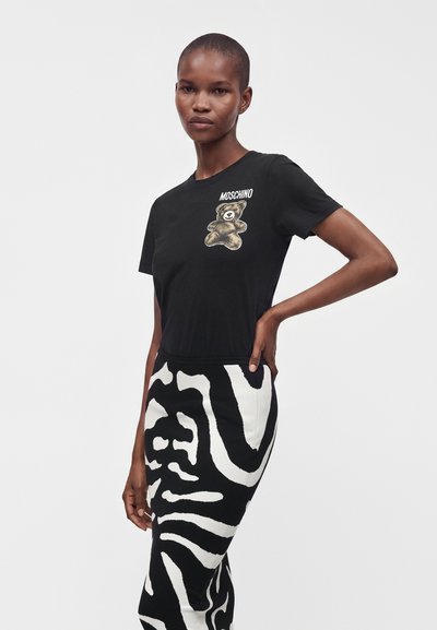Femme portant un t-shirt noir Moschino avec un motif d’ours en peluche et une jupe taille haute imprimée zèbre noir et blanc.