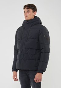 Giacca a vento nera con colletto alto, due tasche sul petto e una tasca sulla manica. Presenta un design trapuntato e polsini elasticizzati.