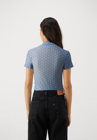 Blå, kortärmad, kort topp med mönstrad design, i kombination med högmidjade svarta jeans med bakfickor och en logotypetikett.