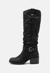 Bottes noires montantes jusqu'aux genoux avec un design relâché, fabriquées en matériau doux. Comprend une sangle décorative perforée et un talon épais.