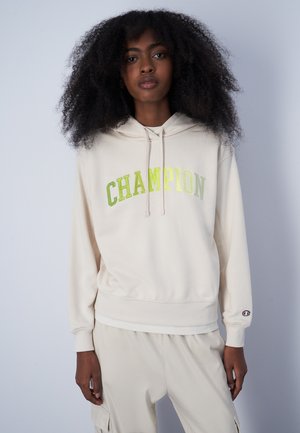 Felpa beige con la scritta "CHAMPION" in lettere verde metallico, cappuccio con cordoncino, polsini e vita a coste, realizzata in morbido tessuto.