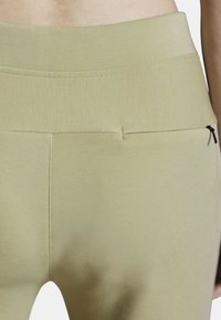 Tapered leggings in pale green stretch fabric, featuring a high waistband and a rear zip pocket, with a smooth texture and subtle sheen.