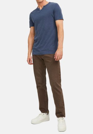 Blå t-shirt med korte ærmer og henley-krave, parret med brune denimjeans og hvide sneakers. Glat tekstur, casual design.