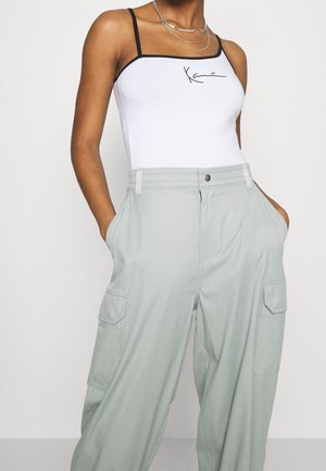 Body blanco con tirantes negros y logo, combinado con pantalones cargo verde claro que tienen bolsillos laterales y un corte holgado.