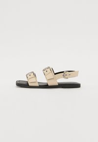Sandale plate bej cu două curele cu catarame, design minimalist, talpă neagră și textură netedă. Include curea ajustabilă pentru gleznă.