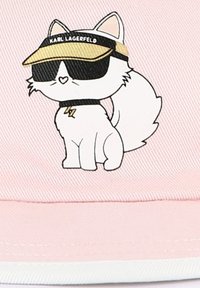 Un chat cartoon blanc avec des accents roses, portant des lunettes de soleil noires et une visière portant l'inscription "KARL LAGERFELD", sur un fond rose.