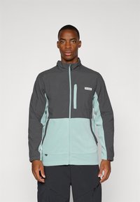 Chaqueta de hombre en gris oscuro y azul claro. Presenta un cierre de cremallera en la parte delantera, collar alto, bolsillo en el pecho y un diseño de paneles en contraste. Material suave, ajuste relajado.