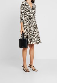 Sukienka kopertowa w panterkę z długimi rękawami, dekoltem w szpic i dopasowaną talią. W połączeniu z czarną torebką i czarnymi sandałkami na obcasie.