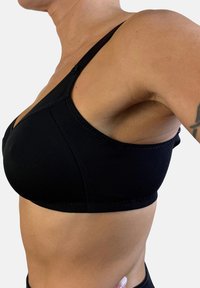 Bralette de tela negra con tirantes ajustables, diseño sin costuras y detalles de costura sutiles. Material suave y elástico para mayor comodidad.