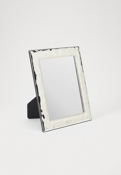 Rama foto metalică cu nuanță argintie și textură ondulată, care susține o oglindă dreptunghiulară. Prezintă un spate întunecat pentru stabilitate.