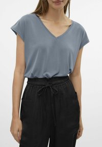 Top de cuello en V, de manga corta en azul claro, hecho de una tela suave. Combinado con pantalones negros de corte holgado que tienen una cinturilla elástica y bolsillos.
